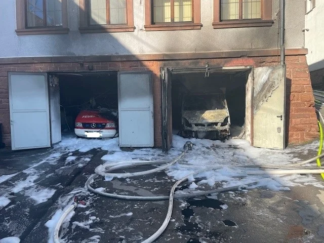 Brandgeschädigte Fahrzeughalle in Frankenstein mit zwei Feuerwehrfahrzeugen, Löschschaum und Schläuchen.