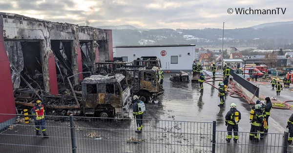 Ausgebrannte Fahrzeughalle in Treffurt mit zerstörten Einsatzfahrzeugen und Feuerwehrleuten.